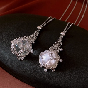 Macro shot of silver dreamcatcher necklace with white pearl and zircon on black satin