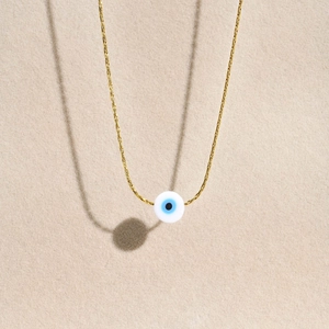 Detailed view of the gold chain and evil eye bead pendant on a textured beige background