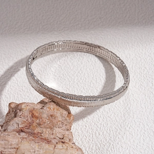 Macro detail of silver geometric bangle with vertical texture on a textured stone base