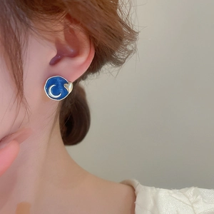 Detailed close-up of blue enamel celestial earring with silver moon and gold heart motifs
