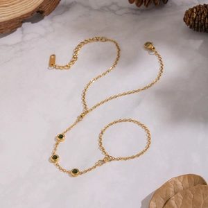 Gold chain slave bracelet featuring three green zircon stones on marble background