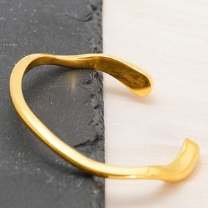 Dettaglio del bracciale aperto irregolare placcato oro 18 carati su sfondo minimalista