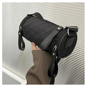 Detail of black cylindrical barrel bag with pleated texture and wide nylon shoulder strap