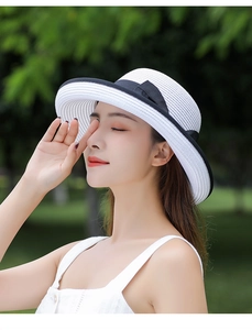 Close-up of white woven straw sun hat featuring a black ribbon bow detail on the brim
