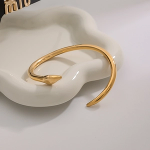 Polished gold snake-shaped stainless steel open bracelet on a white ceramic jewelry tray