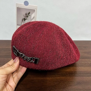 Burgundy knitted beret with sequins and metal chain detail shown on a dark wooden table
