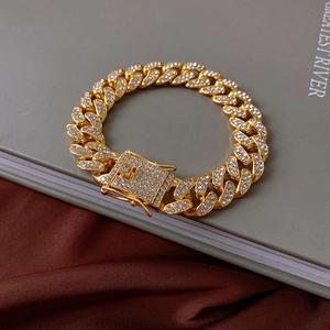 Macro view of gold-plated cuban chain bracelet with pavé rhinestones on satin fabric