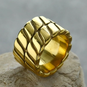Makroaufnahme eines goldfarbenen Rings mit geometrischem Relief auf einer Steinfläche