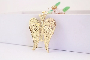 Macro shot of golden metal angel wing charm with textured tree of life centerpiece