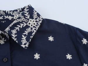 Detail der weißen Stickerei am dunkelblauen Hemdkragen mit schwarzen Knöpfen am Kleid