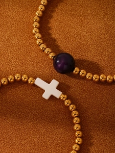 Detailed close-up of beaded stretch bracelets with purple agate sphere and white cross charm