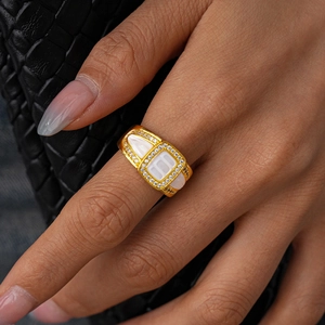 Détail d'une bague dorée avec incrustations de nacre blanche et zircons portée par un mannequin