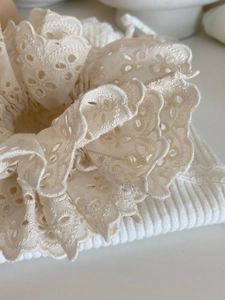 Gros plan sur chouchou en dentelle crème avec motifs floraux ajourés et texture douce en coton