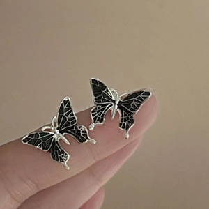 Detail of silver butterfly stud earrings featuring black enamel wings and intricate textures