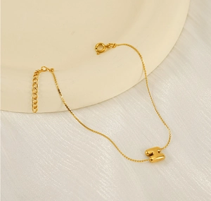 Macro shot of gold stainless steel bracelet with letter H pendant on ceramic dish