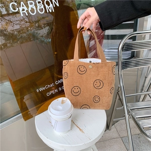 Detailed view of caramel corduroy tote with black smiley embroidery and metal button closure