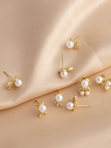 Detailed macro view of gold bear earrings with white pearls on champagne silk fabric