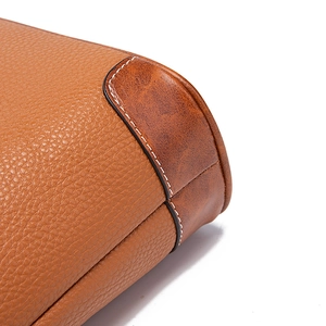 Detail of pebbled litchi grain leather and white stitching on a tan crossbody bag