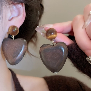 Gros plan de boucles d'oreilles en bois en forme de cœur avec œil de tigre sur l'oreille