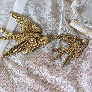 Pair of antique brass swallow wall hangings with detailed feather texture on lace background
