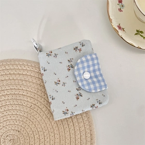 Detailed view of floral wallet with plaid flap and white snap button on woven mat