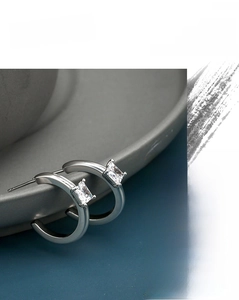 Macro shot of silver C-shaped hoop earrings with square zircon stone in claw setting