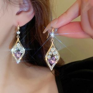 Macro shot of gold square earrings featuring a purple heart crystal and micro-pave zircons