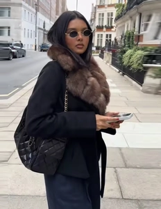 Detail view of stylish black coat featuring a brown faux fur collar and quilted handbag