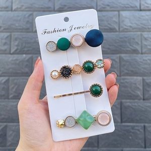 Detail of four candy-colored hair clips with green resin and pearls on a card