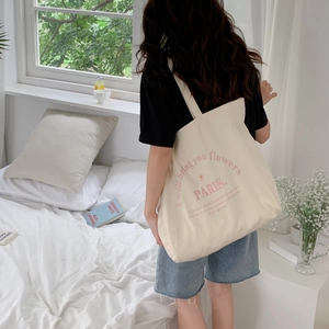 Detailed shoulder view of large canvas tote bag with pink flower embroidery in bedroom