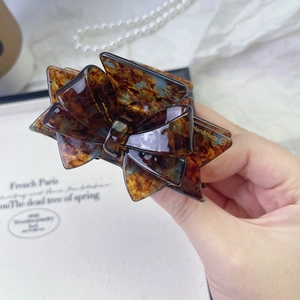 Macro view of a brown tortoiseshell acetate bow hair claw clip with handmade engraving