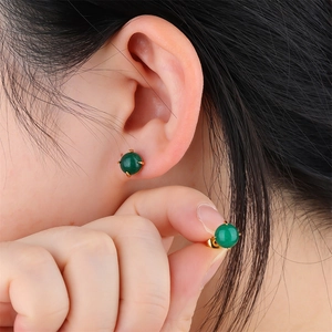 Close-up of golden stud earrings with green spherical stones worn by a model