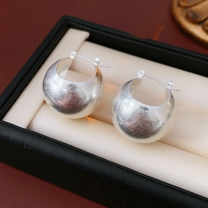 Close-up of silver C-shaped hoop earrings resting on a beige cushion in a black jewelry box