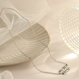 Silver leaf necklace with green stones elegantly placed on a white ceramic plate