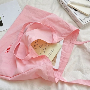 Flat lay of a large pink canvas tote bag with red lettering on a textured white fabric
