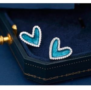 Macro detail of teal enamel heart earrings with pavé stones in a blue velvet box