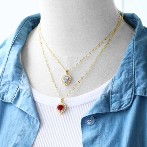 Detail of double-layer gold necklace featuring red and white heart pearls on a mannequin