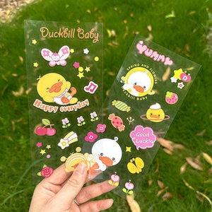 Detail of two transparent PET stickers featuring cute yellow cartoon ducks on a lawn background