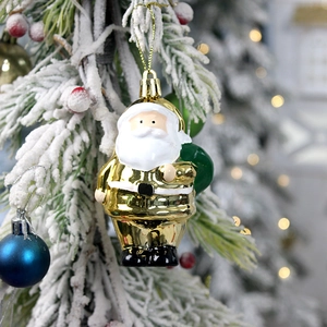 Detail of Santa Claus ornament with gold finish hanging on snowy Christmas tree branch
