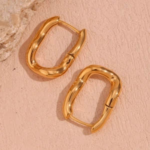 Macro detail of irregular gold U-shaped earrings on elegant beige textured background