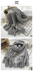 Detail of light gray pleated scarf with fringe on white fabric and woven basket