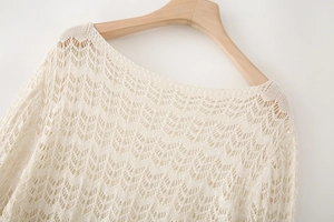 Detail of beige hollow-out crochet knit sweater showing intricate shell pattern on a hanger