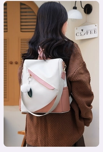 Close-up of color-block women backpack with fluffy ball charm on a model in a cafe