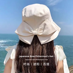 Detail of cream canvas sun hat featuring a large decorative bow on the back against sea