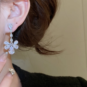 Macro shot of flower-shaped zircon drop earrings with silver metallic finish on model