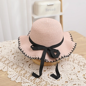 Pink straw sun hat for girls with a black ribbon bow and scalloped edges on lace tablecloth