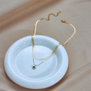 Double-layered gold snake chain necklace with square turquoise pendant on beige silk fabric