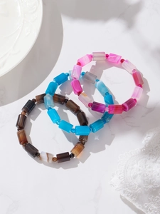 Detailansicht von drei bunten Naturstein-Armbändern auf einem weißen Marmorhintergrund