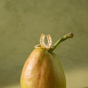 Goldener Hufeisenring mit weißer Perlmutt-Einlage auf kreativem grünem Birnenhintergrund