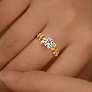 Elegant gold laurel leaf ring with a round moissanite center stone on model hand